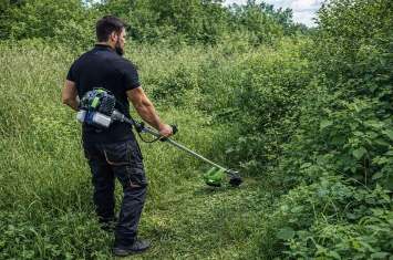Clearing tall grass with a petrol brushcutter in the field